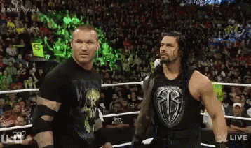 Two Wrestlers Are Standing Next To Each Other In A Wrestling Ring With A Crowd In The Background . GIF