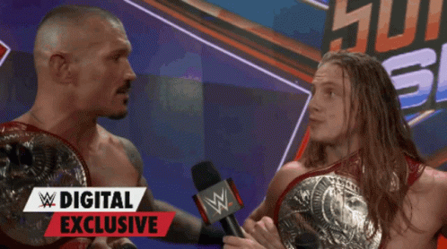Two Wrestlers Are Talking In Front Of A Digital Exclusive Banner GIF