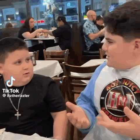 Two Young Boys Are Sitting At A Table In A Restaurant Talking . GIF
