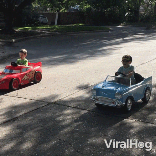 Two Young Boys Driving Toy Cars on Street