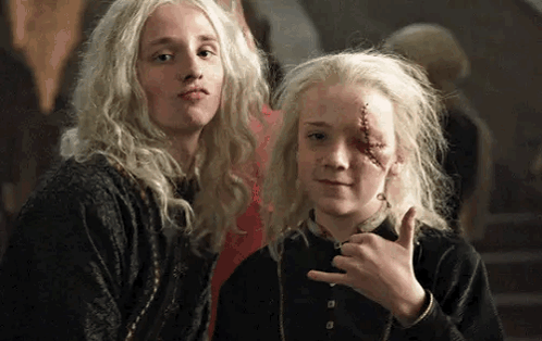 Two Young Girls With Blonde Hair Are Standing Next To Each Other . One Of The Girls Has A Scar On Her Face . GIF