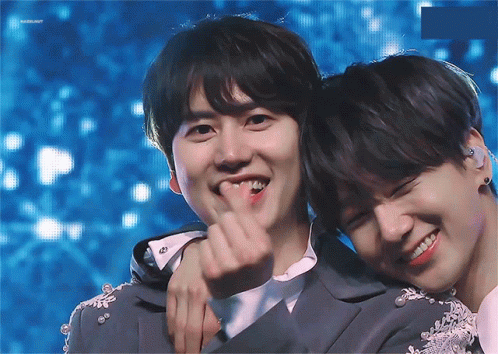 Two Young Men Are Hugging Each Other And One Of Them Is Making A Heart Shape With His Finger GIF