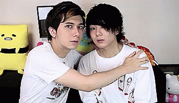 Two Young Men Are Hugging Each Other In Front Of A Hello Kitty Doll . GIF