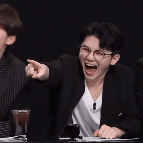 Two Young Men Are Sitting At A Table Laughing And Pointing At Something . GIF