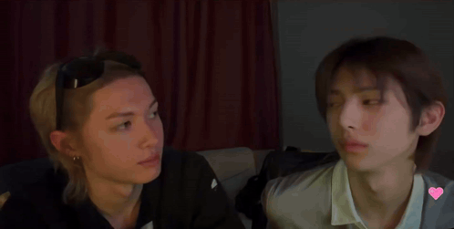 Two Young Men Are Sitting Next To Each Other And Looking At Each Other In A Dark Room . GIF