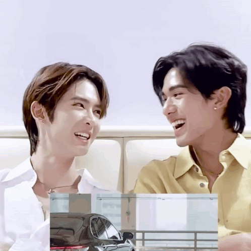 Two Young Men Are Sitting Next To Each Other And Smiling GIF