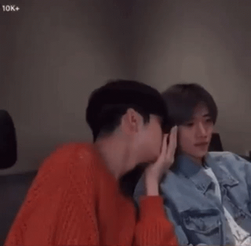 Two Young Men Are Sitting Next To Each Other In A Room And Holding Hands . GIF
