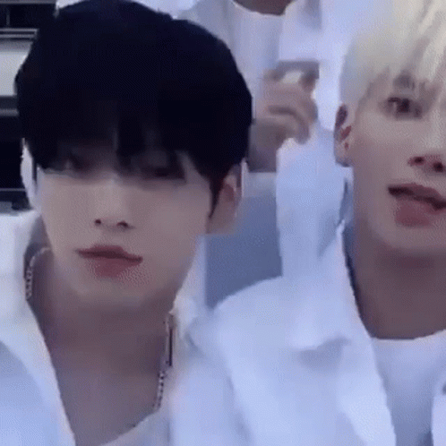 Two Young Men Are Sitting Next To Each Other In A Room And One Of Them Is Wearing A White Shirt . GIF