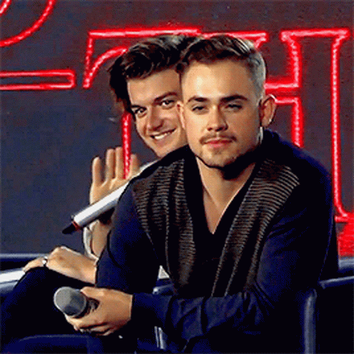 Two Young Men Are Sitting Next To Each Other In Front Of A Microphone . GIF