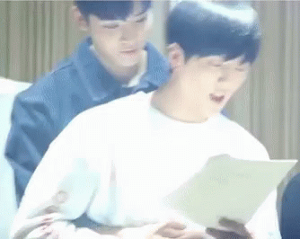 Two Young Men Are Sitting Next To Each Other On A Couch And One Of Them Is Reading A Book . GIF