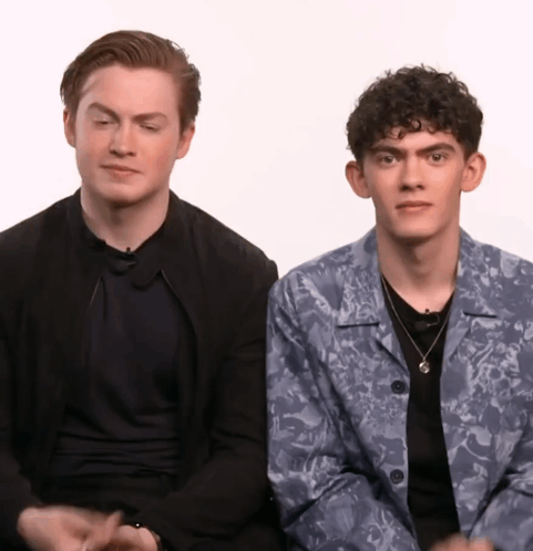 Two Young Men Are Sitting Next To Each Other With One Wearing A Floral Jacket GIF