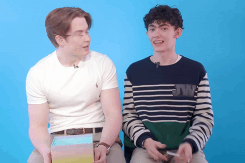 Two Young Men Are Sitting Next To Each Other With One Wearing A Sweater With Jw On It GIF