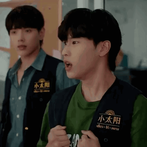 Two Young Men Are Standing Next To Each Other And One Is Wearing A Vest With Chinese Writing On It . GIF