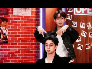 Two Young Men Are Standing Next To Each Other In Front Of A Red Brick Wall . GIF
