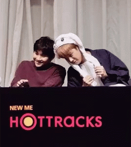 Two Young Men Are Standing Next To Each Other In Front Of A Sign That Says Hottracks GIF