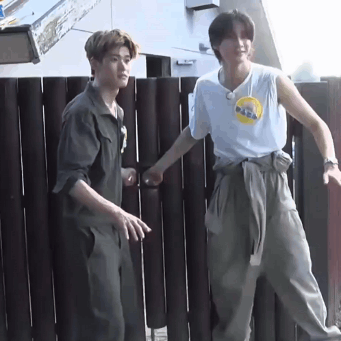 two young men are standing next to each other in front of a wooden fence with one wearing a nasa shirt