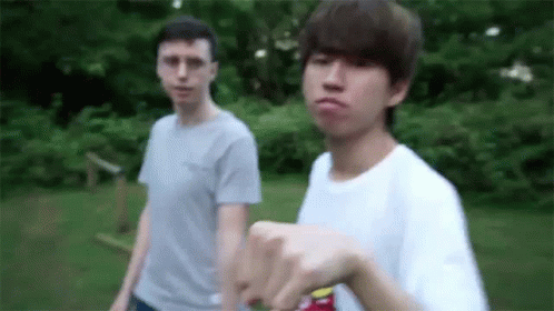 Two Young Men Are Standing Next To Each Other In The Grass . One Of The Men Is Pointing At The Camera . GIF