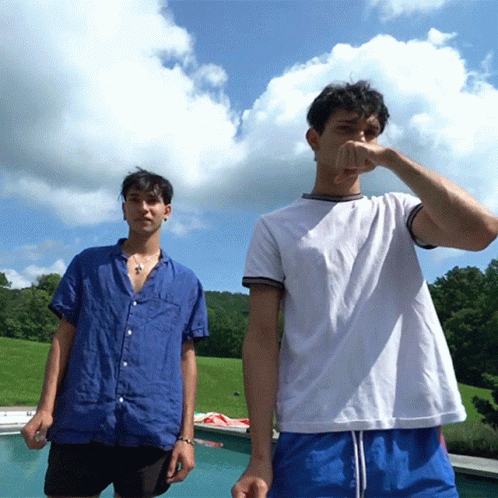 Two Young Men Are Standing Next To Each Other Near A Pool GIF