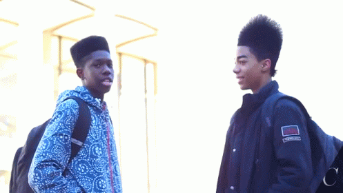 Two Young Men Standing Next To Each Other With One Wearing A Jacket That Has The Word Converse On It GIF