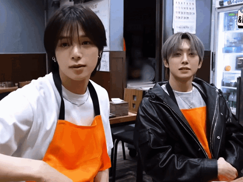 Two Young Men Wearing Aprons Are Standing Next To Each Other In Front Of A Fridge That Says ' Coca Cola ' On It GIF