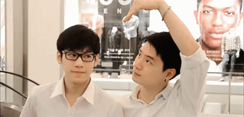 Two Young Men Wearing Glasses Are Standing Next To Each Other And Making A Heart Shape With Their Hands . GIF