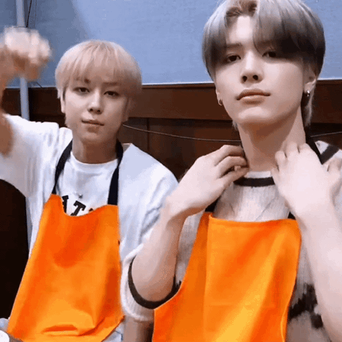 Two Young Men Wearing Orange Aprons Are Posing For A Picture Together . GIF