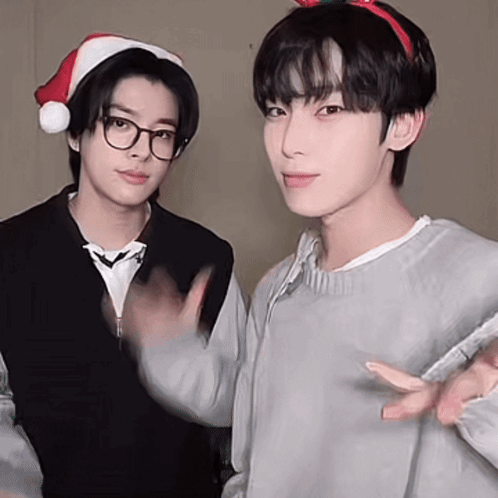 Two Young Men Wearing Santa Hats Are Standing Next To Each Other . GIF