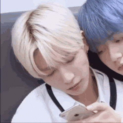 Two Young Men With Blonde Hair And Blue Hair Are Sitting Next To Each Other And Looking At A Cell Phone . GIF