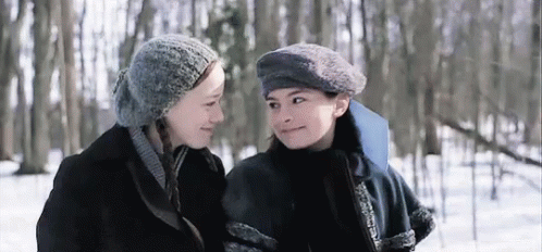 Two Young Women Are Standing Next To Each Other In The Snow And Looking At Each Other . GIF