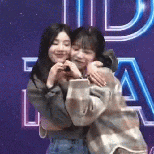 Two Young Women Hugging In Front Of Purple Sign GIF
