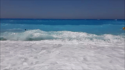 Waves Crashing Against A Sandy Beach With A Person In The Water GIF