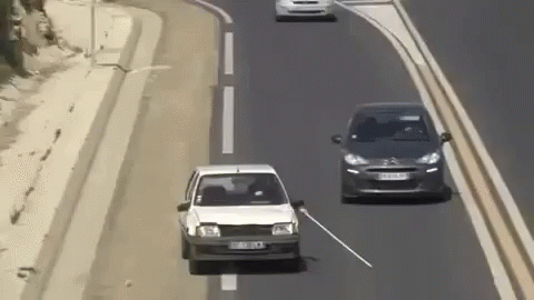 White Car Driving Next to Black Car With Stick Out Window