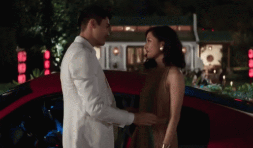 White Suit Man and Brown Dress Woman Holding Hands Red Car