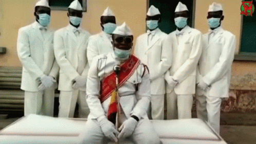 White Suited Men With Masks Around White Coffin GIF