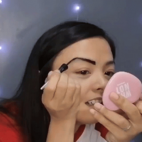 Woman Applying Makeup To Eyebrows In Pink Mirror GIF