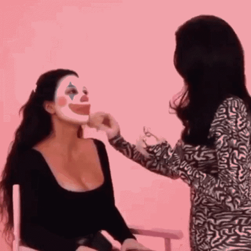 Woman Applying Makeup to Woman with Clown Mask