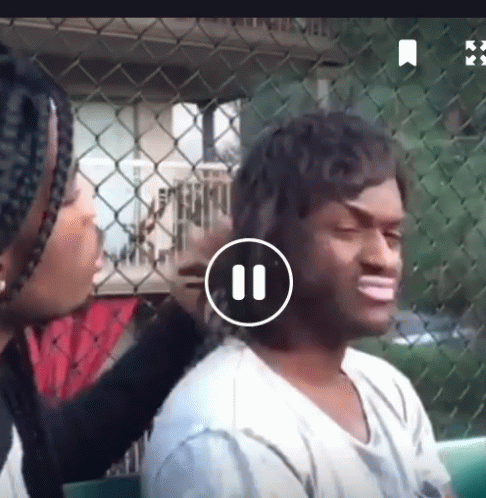 Woman Brushing Man's Hair in Front of Chain Link Fence Playing Video