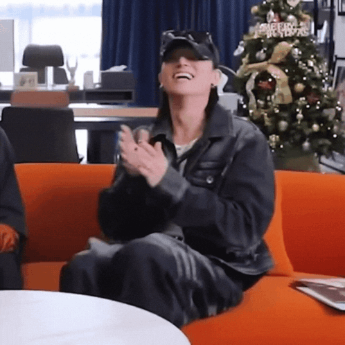 Woman Clapping on Orange Couch by Christmas Tree