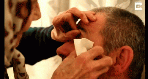 Woman Cleaning Man's Eye With Paper GIF