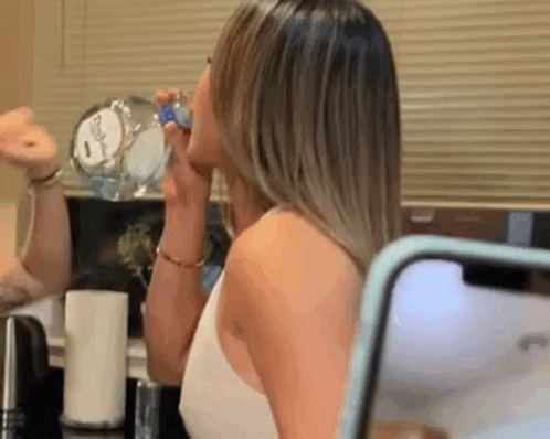 Woman Drinking Water From Bottle Looking at Phone in Mirror