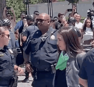 Woman Escorted By Police Officer As Crowd Takes Pictures GIF