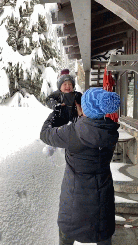 Woman Holding Baby In Front Of Snowy Building GIF