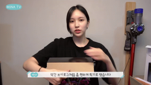 Woman Holding Box In Front Of Mina TV Sign GIF