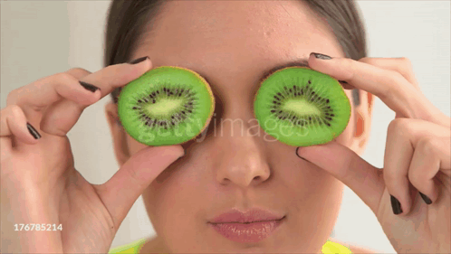 Woman Holding Kiwi Slices in Front of Eyes