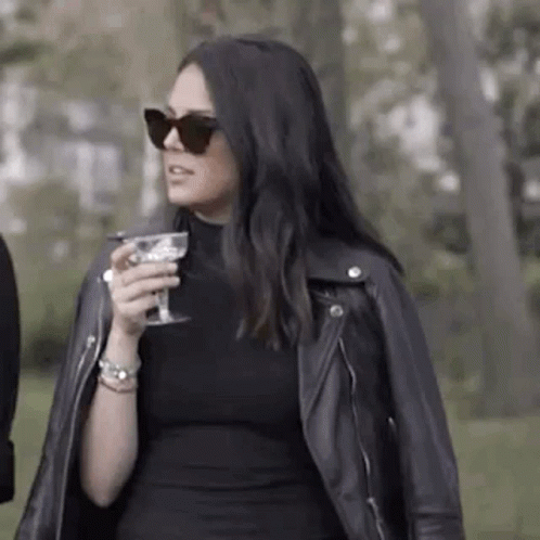 Woman In Black Dress And Leather Jacket Holding Wine GIF