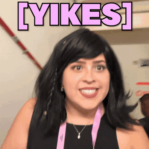 Woman in Black Dress and Pink Lanyard Smiling Beside Yikes Sign