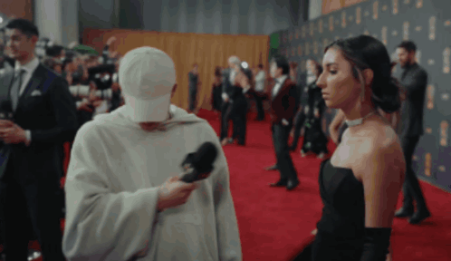 Woman in Black Dress Interviewed by Man in White Hat on Red Carpet