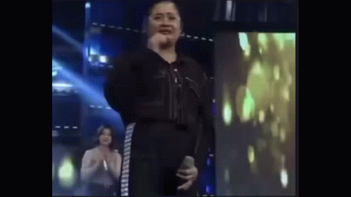 Woman In Black Jumpsuit Holding Microphone On Stage GIF