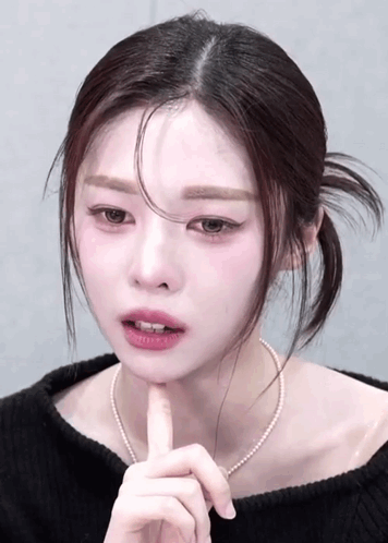Woman In Black Sweater And Pearl Necklace Touching Chin GIF