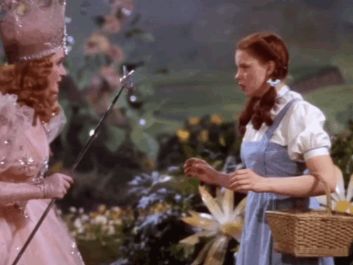 Woman In Blue Dress Beside Woman In Pink Dress With Wand GIF